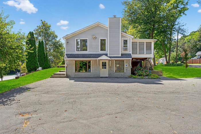 View of front of property with stairway, a front yard, a shingled roof, a chimney, and a patio area