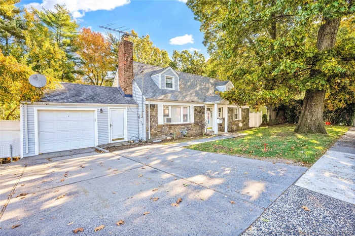 New england style home with concrete driveway, stone siding, a chimney, an attached garage, and a shingled roof