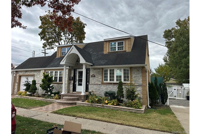 Cape cod house featuring stone siding, an attached garage, and a shingled roof