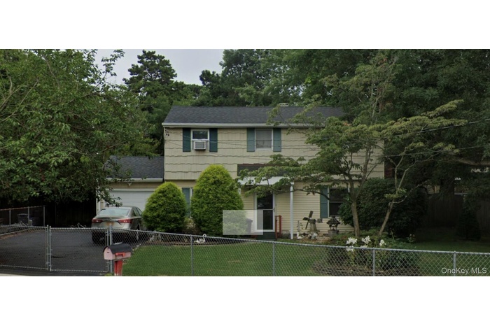 Colonial home with a fenced front yard, roof with shingles, an attached garage, driveway, and view of wooded area