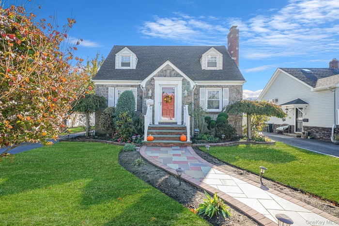 Cape cod house with stone siding, a chimney, and a front yard