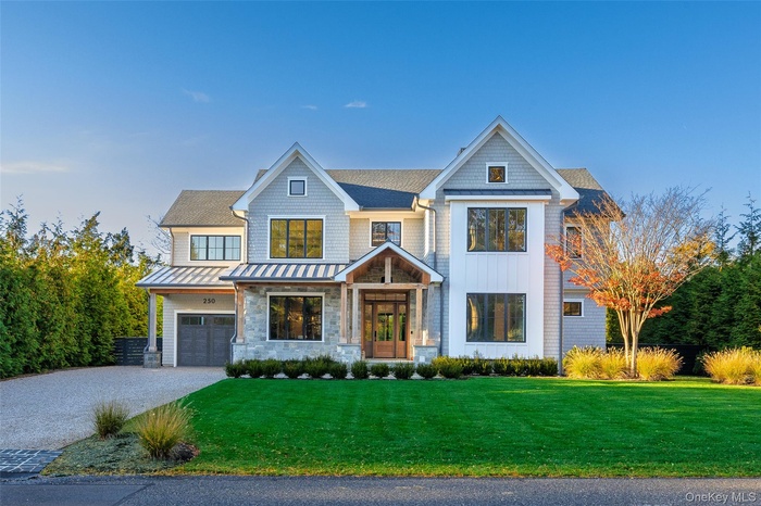View of front facade featuring driveway, a front lawn, a standing seam roof, a metal roof, and stone siding