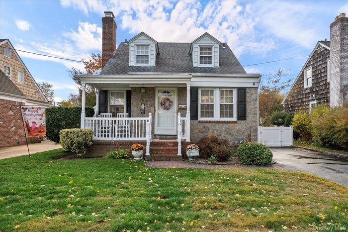 View of front facade featuring stone siding, a porch, a chimney, roof with shingles, and a gate