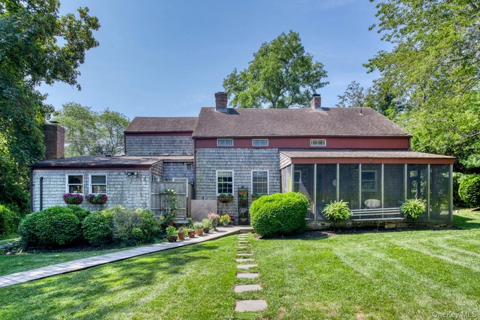 Rear view of property featuring a yard, a chimney, a sunroom, and roof with shingles