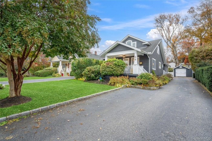 View of front facade featuring a front lawn, a garage, an outbuilding, covered porch, and driveway