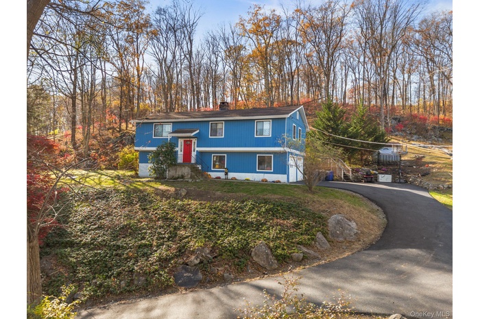 Raised ranch with driveway, a chimney, view of wooded area, and a garage