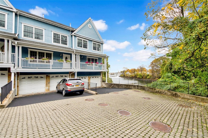 View of front of property with asphalt driveway, an attached garage, a water view, and a balcony