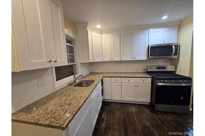 Kitchen with appliances with stainless steel finishes, white cabinets, backsplash, dark wood finished floors, and recessed lighting