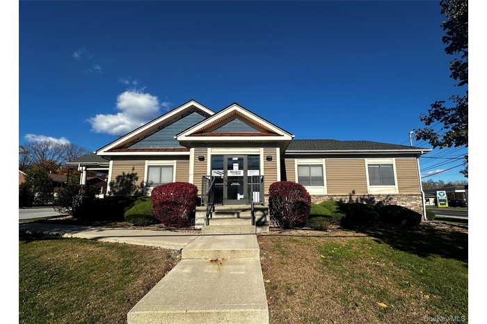 View of front of house with a front yard, stone siding, and a shingled roof