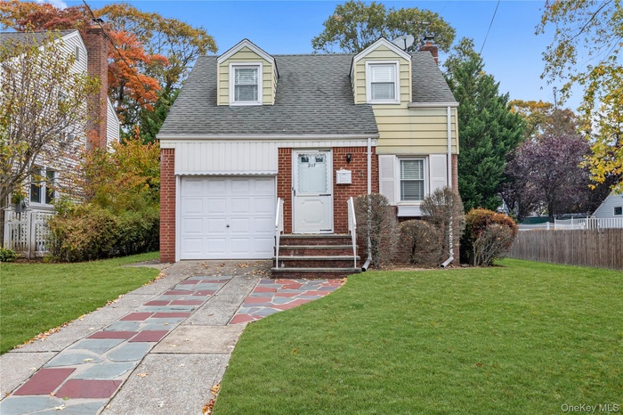 Cape cod-style house with roof with shingles, brick siding, a chimney, and a garage