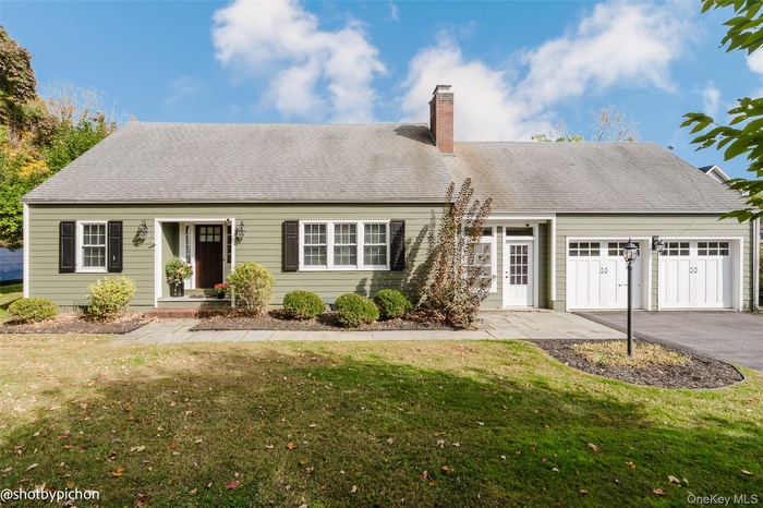 Cape cod-style house with a front lawn, a garage, a chimney, and roof with shingles