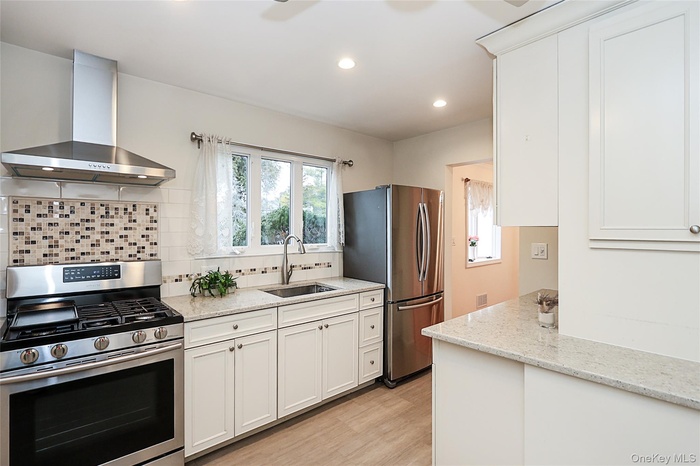 Kitchen featuring stainless steel appliances, wall chimney range hood, white cabinetry, plenty of natural light, and recessed lighting