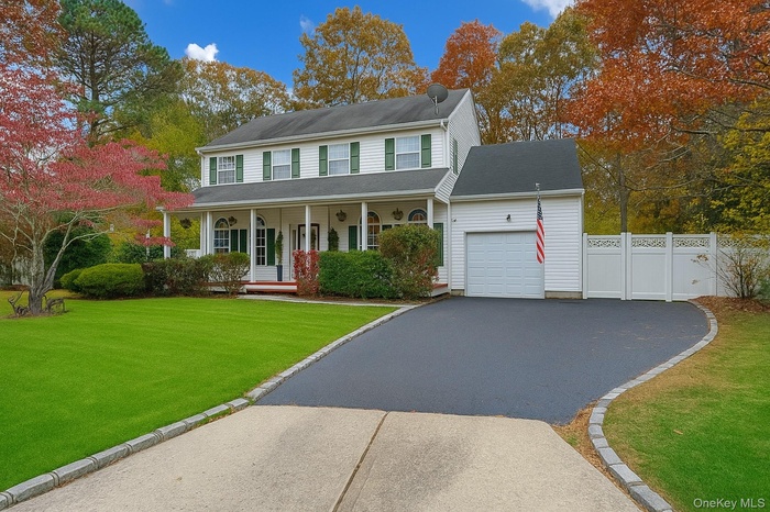 Colonial home featuring covered porch, driveway, an attached garage, and a gate