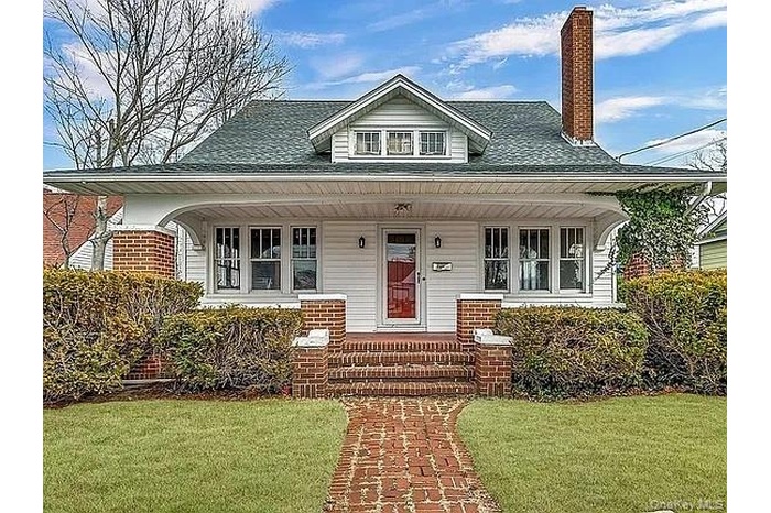 View of front of house with covered porch, a chimney, a shingled roof, and a front yard