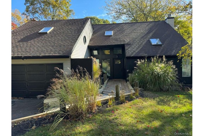 View of front of home with a chimney, a shingled roof, a garage, and a front lawn