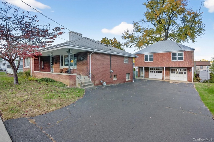 View of front facade featuring brick siding, covered porch, asphalt driveway, and a chimney