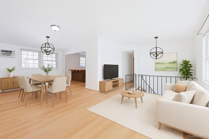 Living area featuring a chandelier, light wood-style flooring, and an AC wall unit(virtual staging)