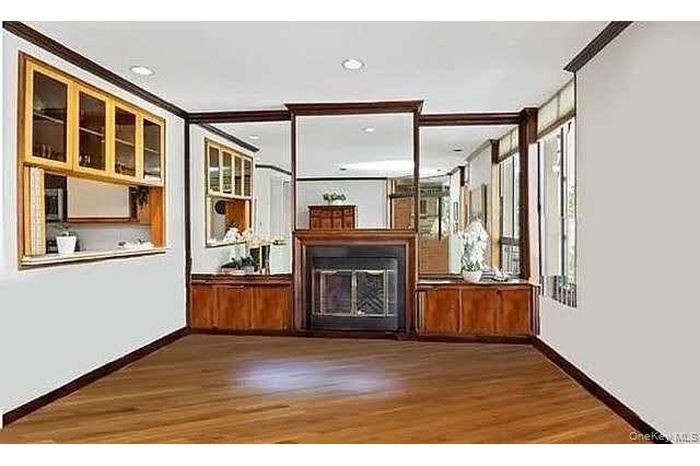 Unfurnished living room featuring a glass covered fireplace, wood finished floors, crown molding, and recessed lighting