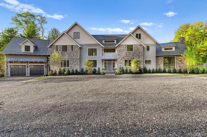 View of front of house with stone siding, chimney, new plantings and driveway