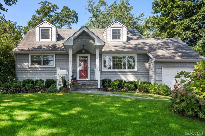New england style home with a front yard, a garage, and a shingled roof