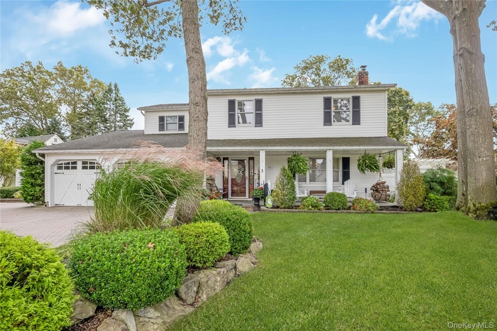 Traditional-style home with a porch, a chimney, a garage, a front lawn, and roof with shingles