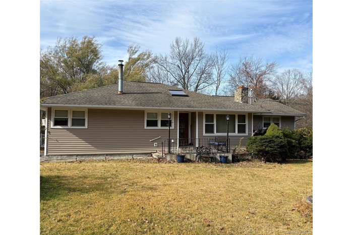View of front of home with a front lawn, a chimney a shingled roof and a covered porch