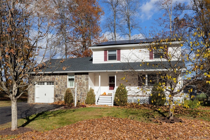 Traditional-style house featuring covered porch, stone siding, roof mounted solar panels, a garage, and driveway