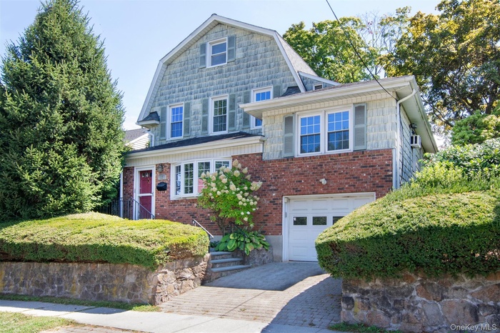 Colonial inspired home featuring a gambrel roof, a garage, driveway, and brick siding