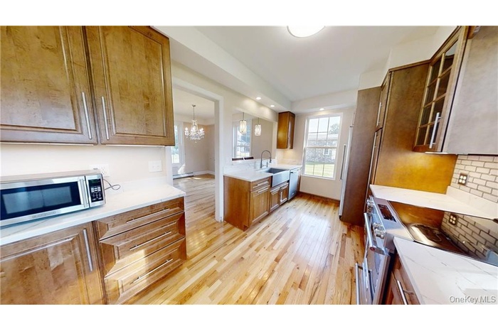 Kitchen featuring glass insert cabinets, appliances with stainless steel finishes, light wood-style floors, brown cabinets, and a chandelier