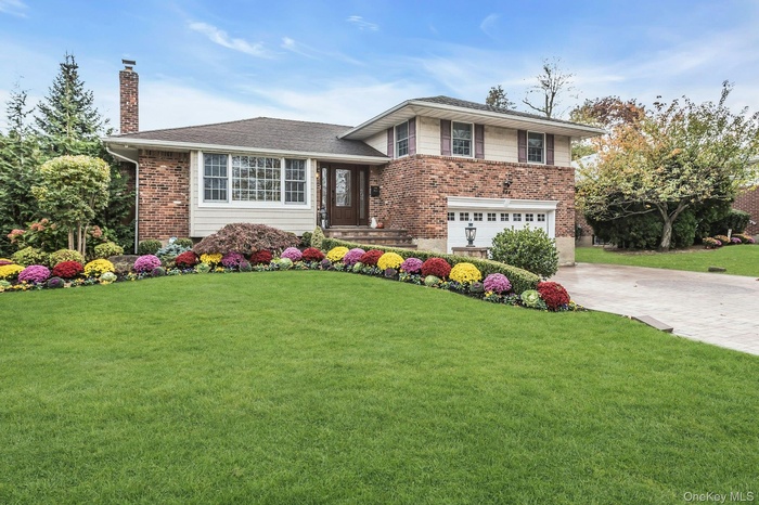 Split level home featuring driveway, a front yard, a chimney, brick siding, and an attached garage