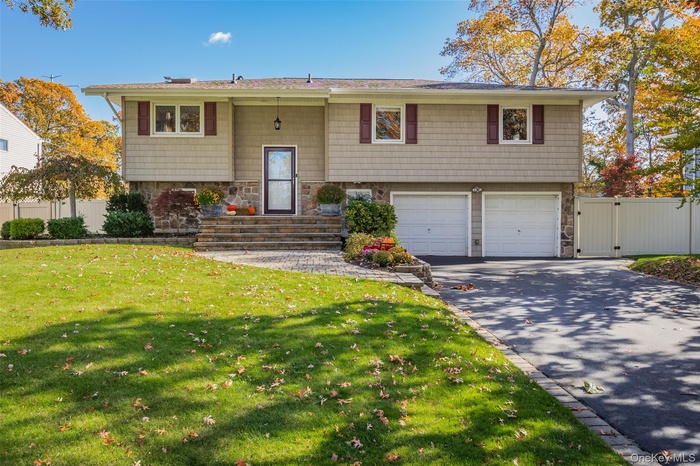 Split foyer home featuring stone siding, an attached garage, a gate, and driveway