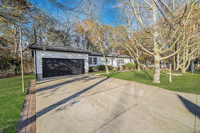 View of front facade featuring a front yard, concrete driveway, and an attached garage