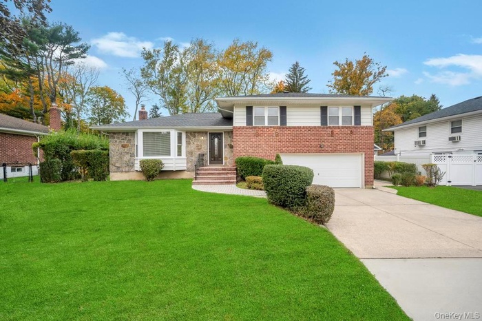 Tri-level home featuring driveway, an attached garage, a chimney, and brick siding