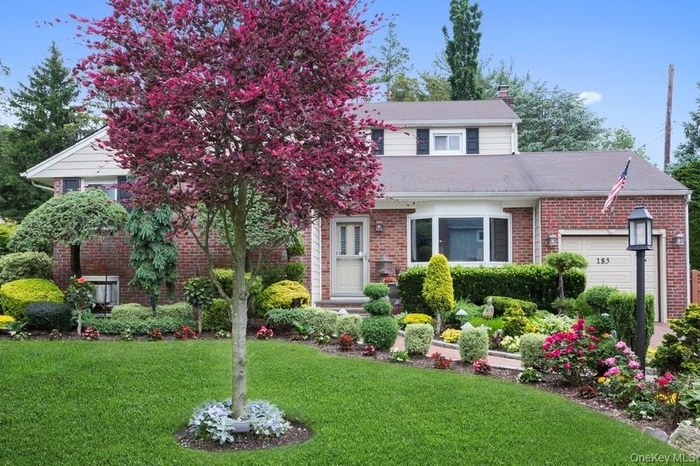 View of front of property with brick siding, a front lawn, an attached garage, and a chimney
