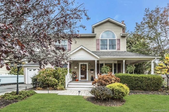View of front facade with a front lawn, covered porch, a garage, and a chimney
