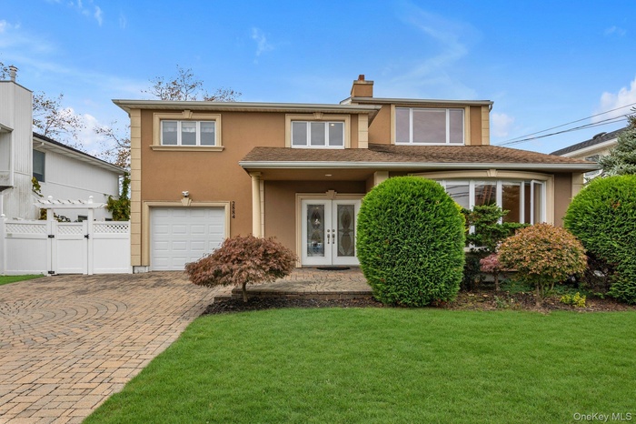 View of front of house featuring stucco siding, decorative driveway, a chimney, a garage, and french doors