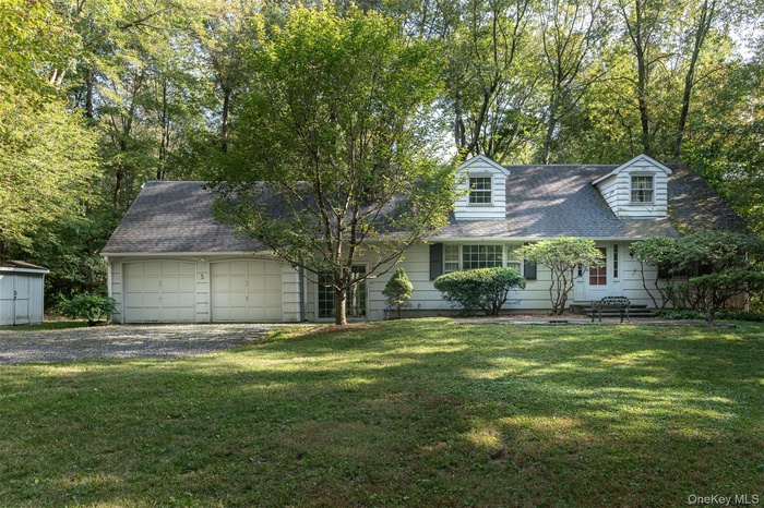 Cape cod-style house with roof with shingles, a front yard, driveway, and an attached garage