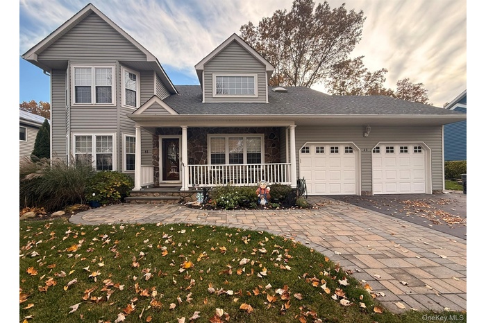 View of front of property featuring a porch, an attached garage, driveway, a front lawn, and stone siding