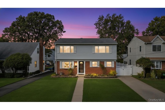 Colonial inspired home featuring brick siding, a chimney, a gate, and driveway