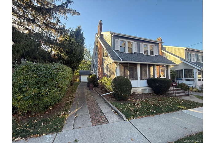 View of front of property with a chimney, a shingled roof, and a sunroom