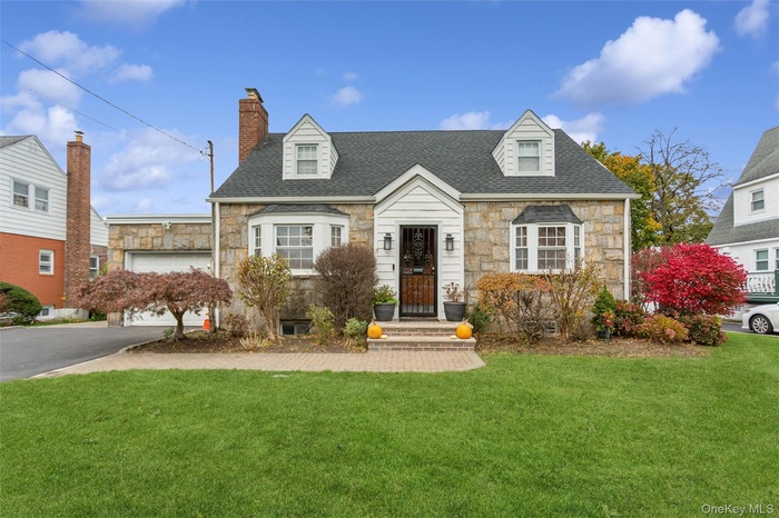 Cape cod home with stone siding, a front lawn, a chimney, and roof with shingles