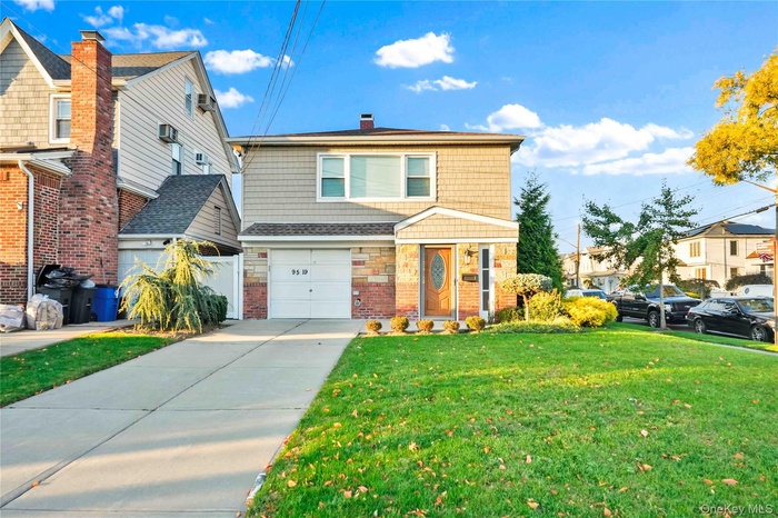 View of front facade featuring a front yard, driveway, a chimney, an attached garage, and brick siding