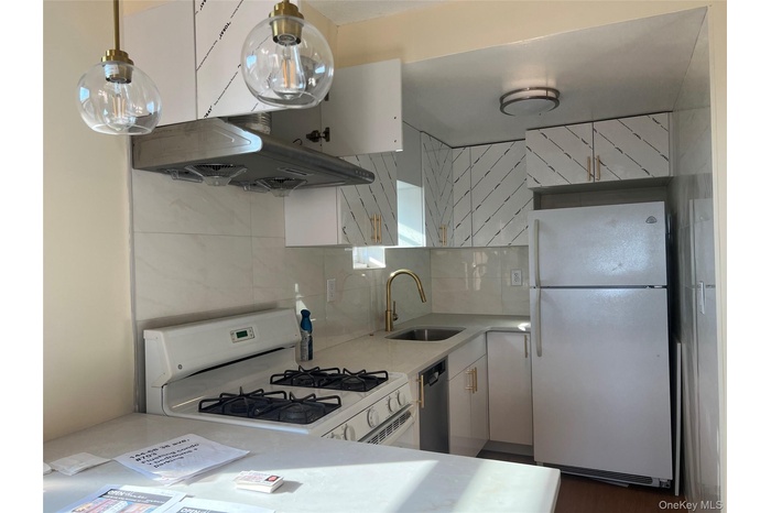 Kitchen with white appliances, decorative backsplash, white cabinets, range hood, and light stone counters