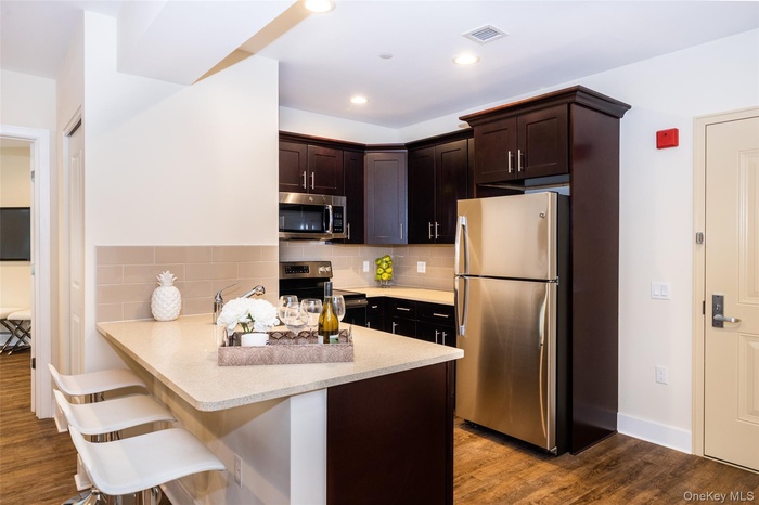 Kitchen featuring a peninsula, dark wood-style flooring, backsplash, appliances with stainless steel finishes, and a breakfast bar