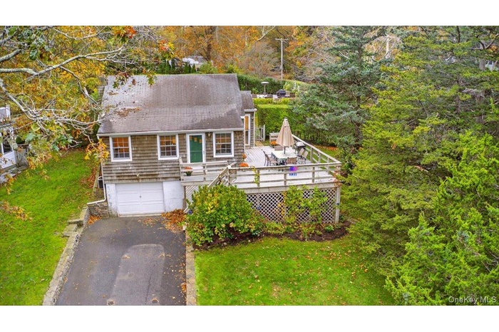 View of front of property featuring asphalt driveway, a wooden deck, roof with shingles, and a front yard