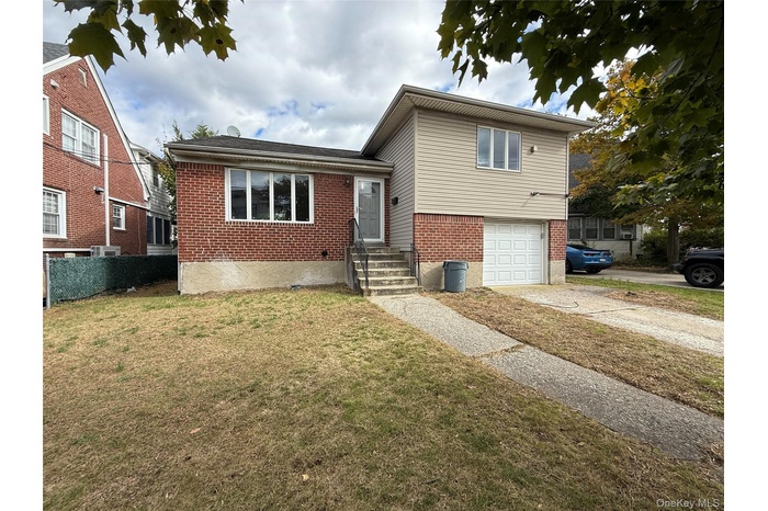 Split level home with brick siding, a garage, driveway, and a front yard