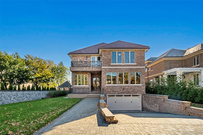 View of front of house featuring a balcony, brick siding, decorative driveway, a tiled roof, and an attached garage