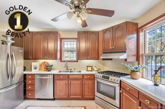 Kitchen with appliances with stainless steel finishes, brown cabinets, light countertops, and under cabinet range hood