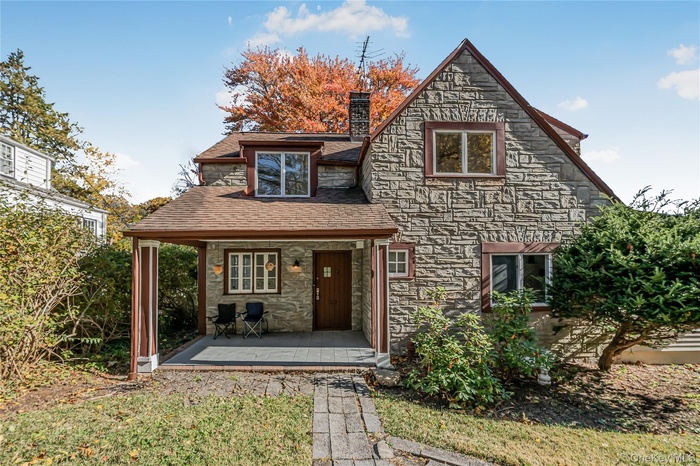 View of front of house with a porch, a chimney, stone siding, and a front yard