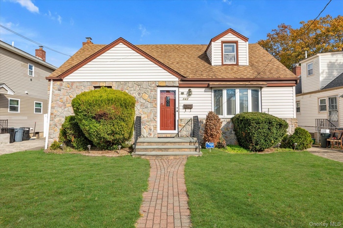 View of front facade with a front yard, stone siding, and a shingled roof
